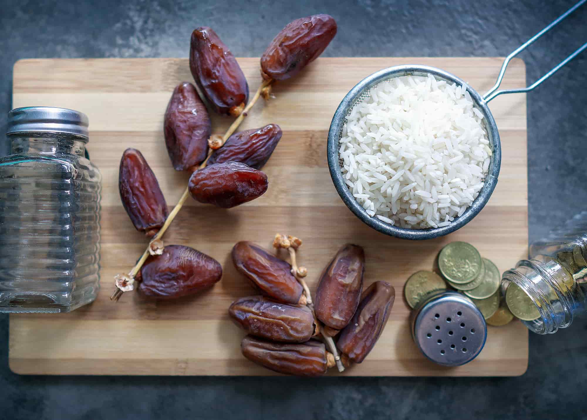 صورة تظهر مفهوم الزكاة في رمضان وتحوي الأرز والتمر وبعض العملات النقدية على رف خشبي